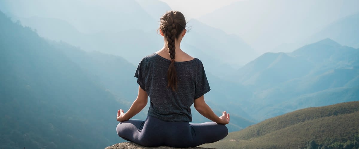 Žena medituje na skále s výhledem na horskou krajinu