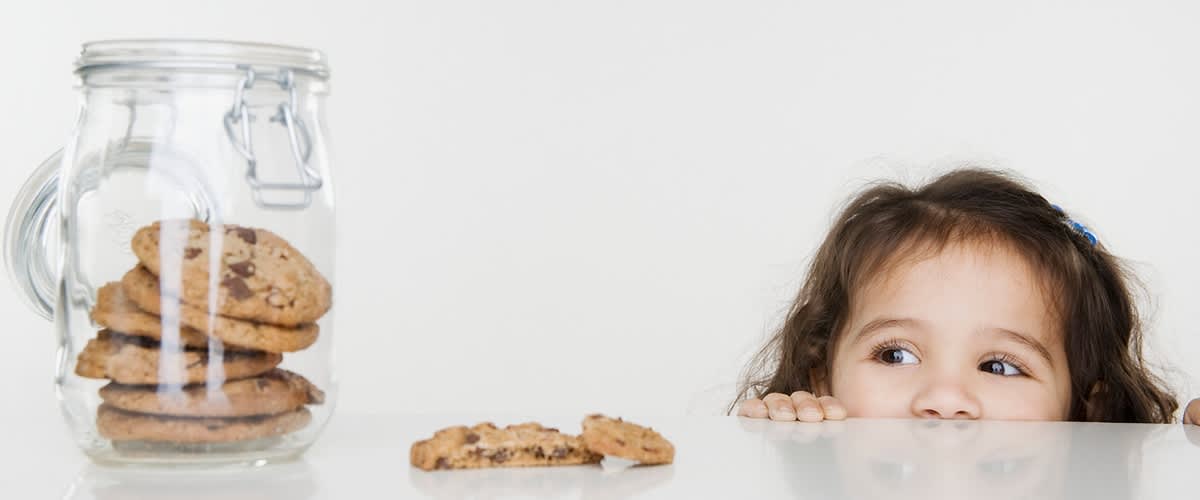 Sklenice s čokoládovými sušenkami a dítě vykukující za stolem