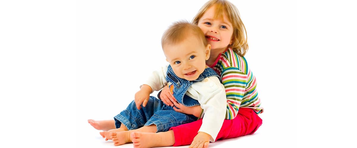 Dvě malé děti sedící na bílém pozadí, jedno v pruhovaném tričku, druhé v džínových lacláčích