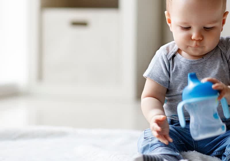 Malé dítě drží modrou dětskou láhev.