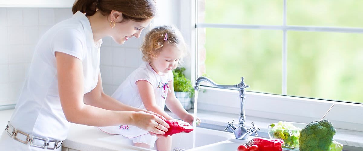 Maminka a dítě myjí zeleninu u kuchyňského dřezu.