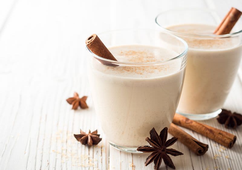 Dva sklenice chai latte s celou skořicí a badyánem na bílém dřevěném stole.