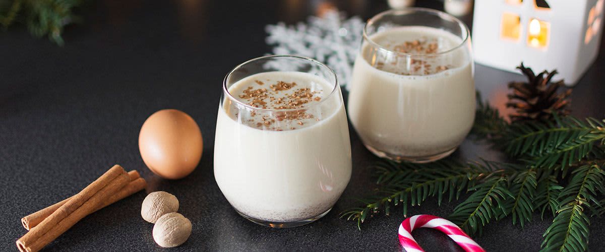 Vánoční nápoj v sklenicích s kořením, vejcem, skořicí a cukrovou tyčinkou na stole