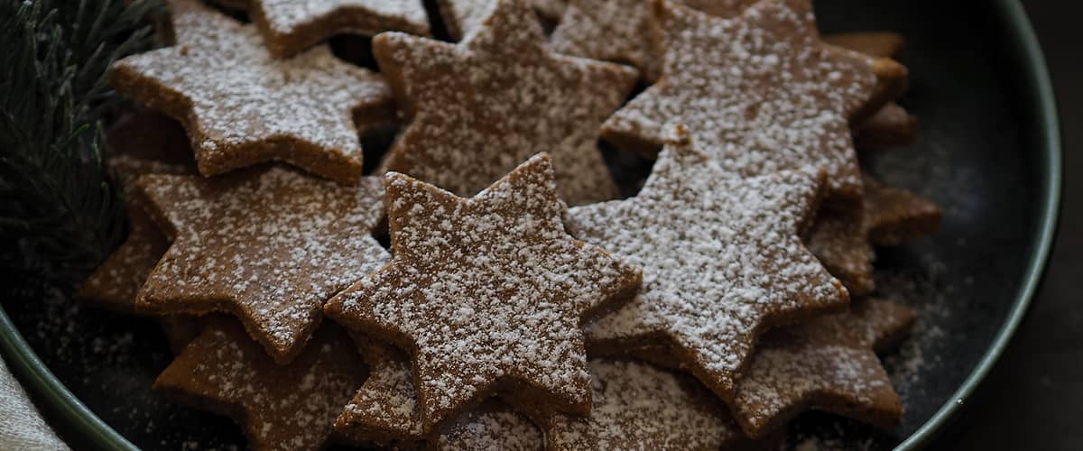 Perníkové hvězdičky posypané cukrem na talíři s větvičkou jehličnanu a rukou dítěte.
