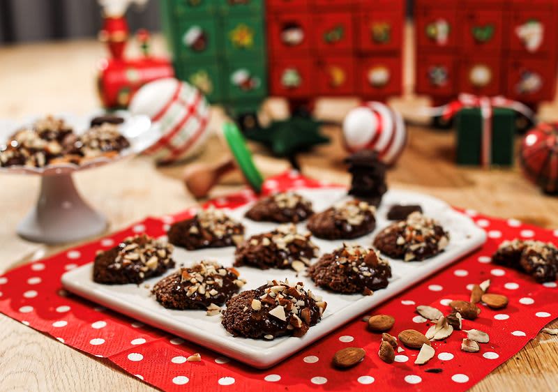 Čokoládové sušenky s oříšky na talíři, vánoční dekorace v pozadí.