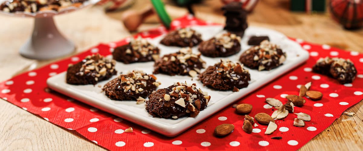 Čokoládové sušenky s oříšky na talíři, vánoční dekorace v pozadí.