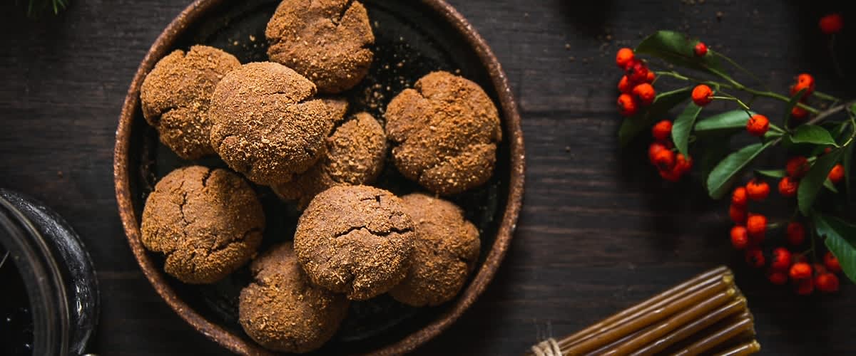 Talíř s domácími sušenkami na dřevěném stole, vedle svazek svíček a červené bobule.