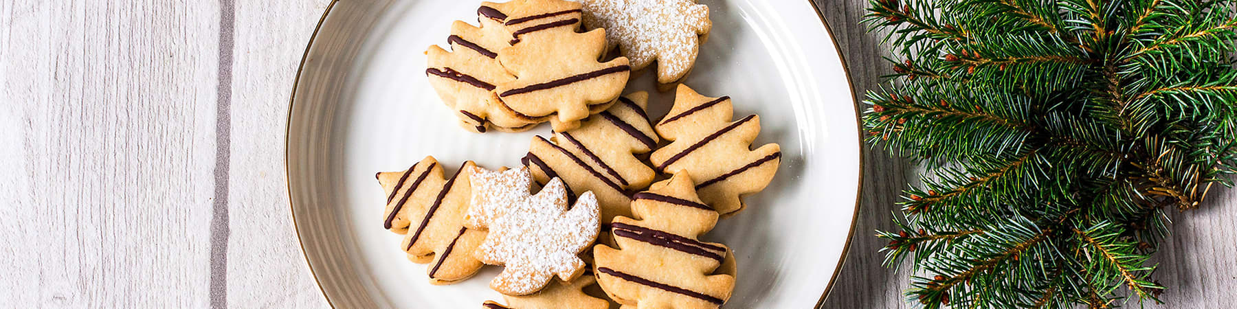 Vánoční cukroví na talíři, šišky a větvička jehličnanu na dřevěném stole