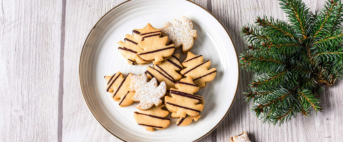 Vánoční cukroví na talíři, šišky a větvička jehličnanu na dřevěném stole