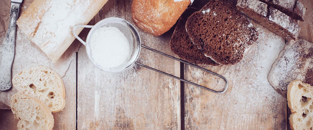 Různé druhy chleba na dřevěném stole s moukou a nožem.