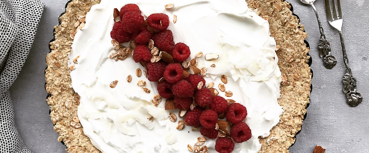 Koláč s krémem, malinami a ořechy na šedém pozadí s vidličkou a lžící