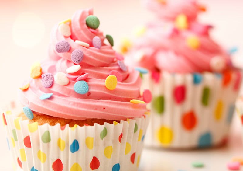 Dva růžové cupcakes s barevnými posypkami v puntíkovaných košíčcích.