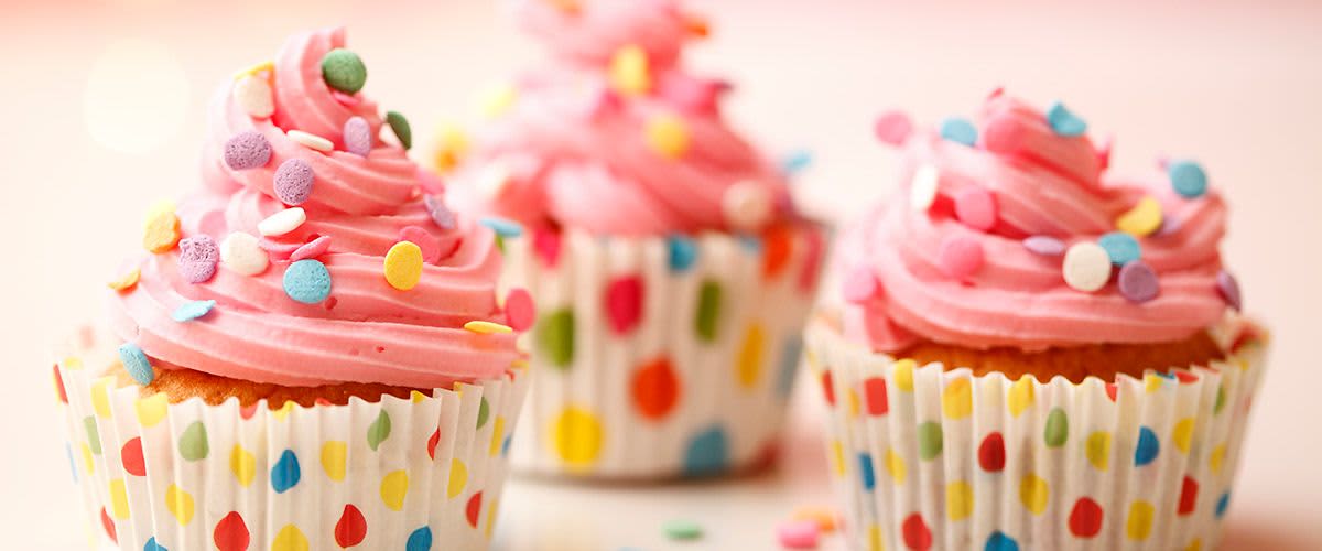Dva růžové cupcakes s barevnými posypkami v puntíkovaných košíčcích.