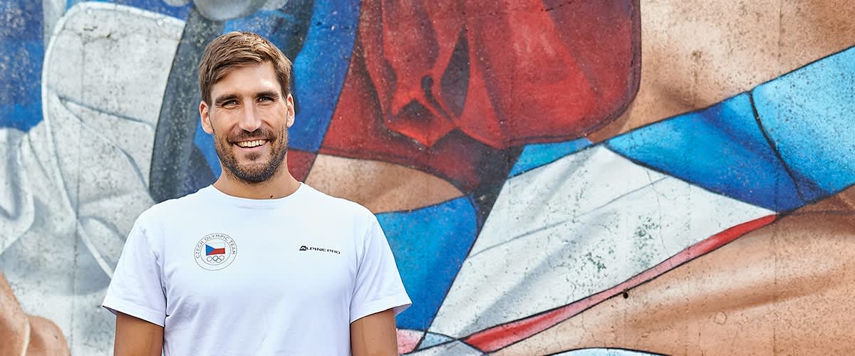 Muž v bílém tričku před barevnou malbou na zdi