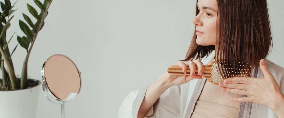 Žena si kartáčuje vlasy dřevěným kartáčem