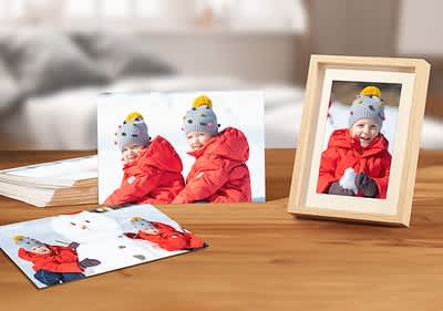 Dítě v červené bundě s čepicí, sněhulák, fotografie na dřevěném stole