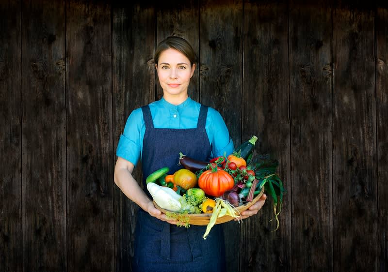 Osoba držící košík plný různých druhů zeleniny před dřevěnou stěnou