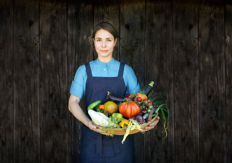 Osoba držící koš plný různorodé zeleniny před dřevěnou stěnou