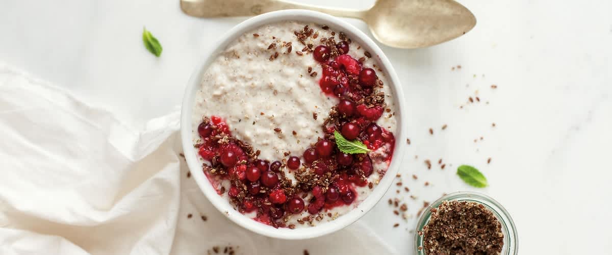 Ovesná kaše s červeným ovocem a lněnými semínky na bílém stole