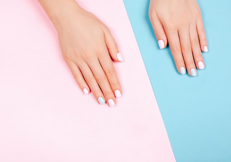Ruce s barevnými nehty na růžovém a modrém pozadí