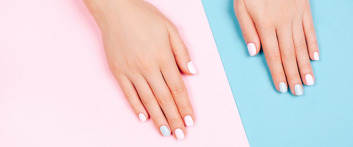 Ruce s pastelově nalakovanými nehty na růžovém a modrém pozadí