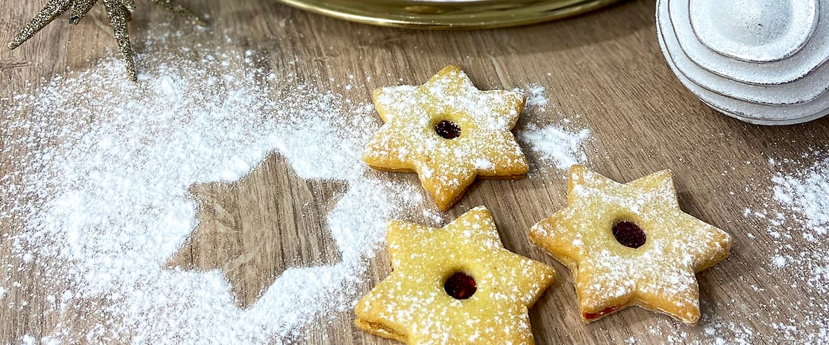 Vánoční cukroví ve tvaru hvězd a srdcí na dřevěném stole, posypané moučkovým cukrem.