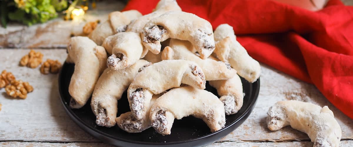 Talíř s vanilkovými rohlíčky, ořechy, květiny a balení špaldové mouky na pozadí