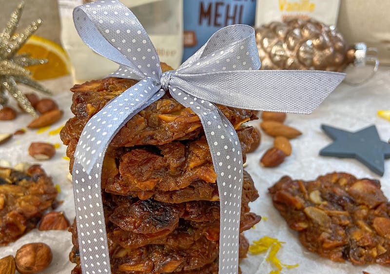 Hromádka ořechových sušenek svázaná stuhou, obklopená ořechy a vánočními dekoracemi