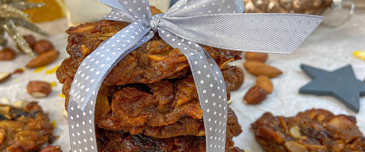 Hromádka ořechových sušenek svázaná stuhou, obklopená ořechy a vánočními dekoracemi