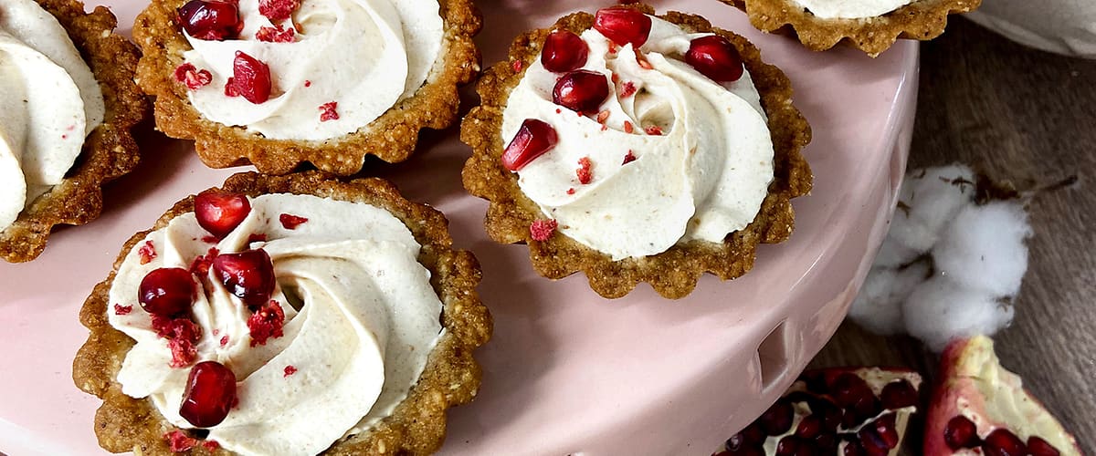 Mini dortíky s krémem a granátovým jablkem na růžovém podnosu, vedle rozkrojené granátové jablko