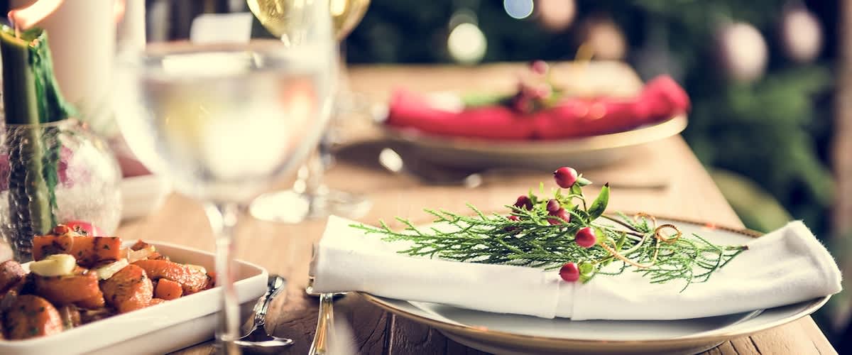 Vánoční stůl s dekorací, sklenicemi vína a talířem s pečenou zeleninou.
