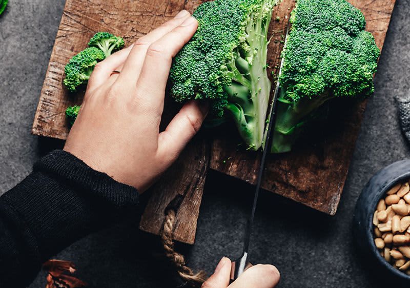 Osoba krájí brokolici na dřevěném prkénku