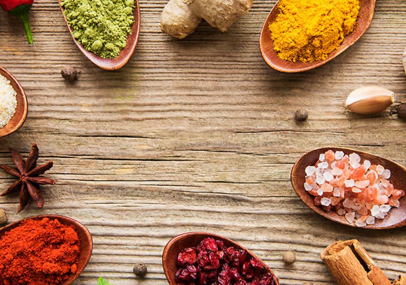 Různé koření na dřevěném stole, včetně kurkumy, soli, zázvoru, papriky a dalších druhů koření.