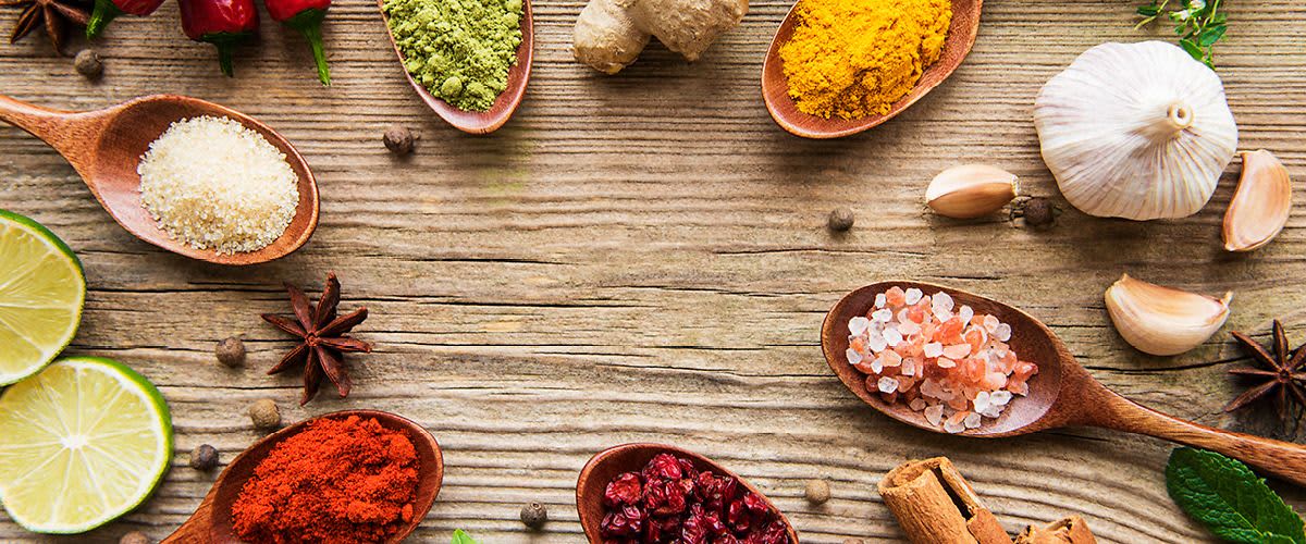 Různé koření na dřevěném stole, včetně kurkumy, soli, zázvoru, papriky a dalších druhů koření.
