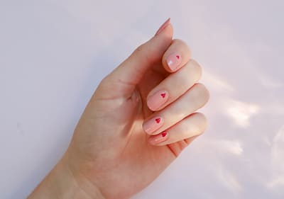 Ruka s růžovými nehty a červenými srdíčky na bílém pozadí