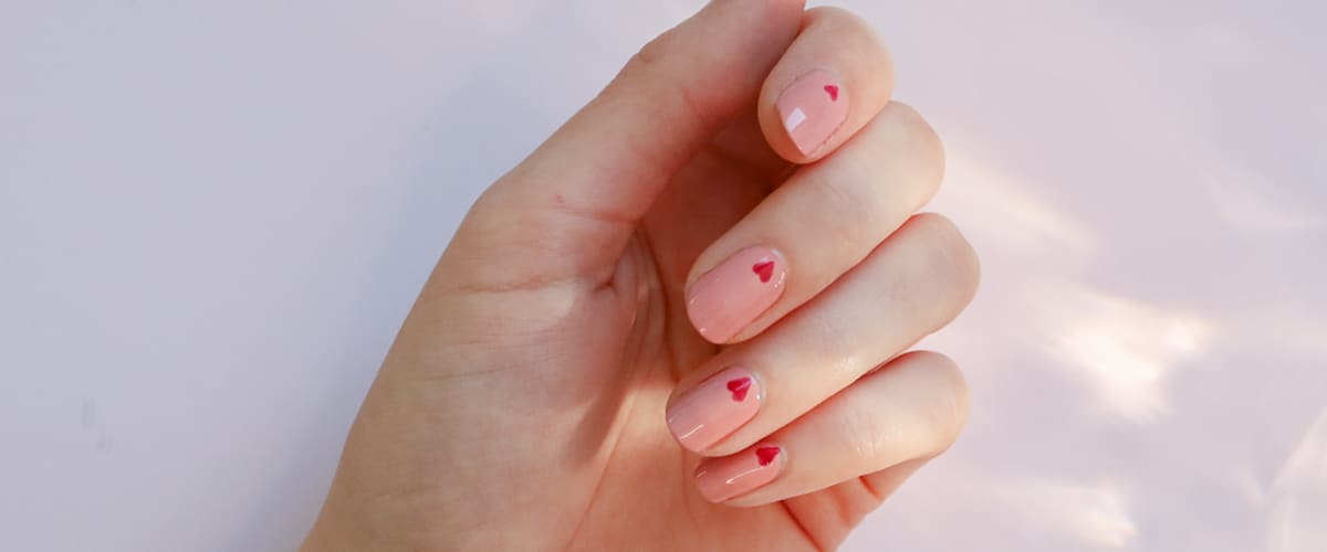 Ruka s růžovými nehty a červenými srdíčky na bílém pozadí