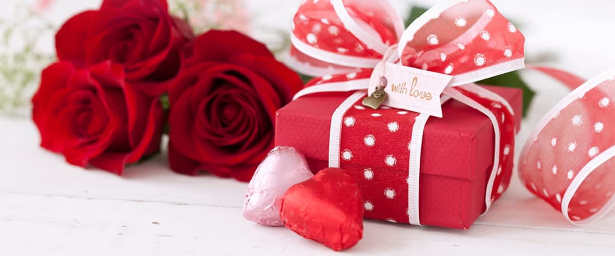 Červené růže a dárková krabička s mašlí na bílém pozadí