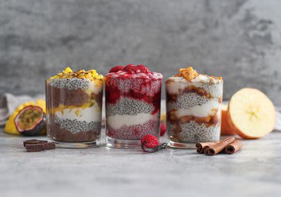 Tři sklenice chia pudinku s ovocem: mango, maliny, jablka a skořice na šedém pozadí