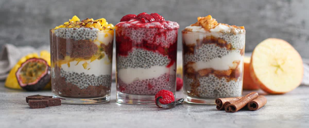 Tři sklenice chia pudinku s ovocem: mango, maliny, jablka a skořice na šedém pozadí