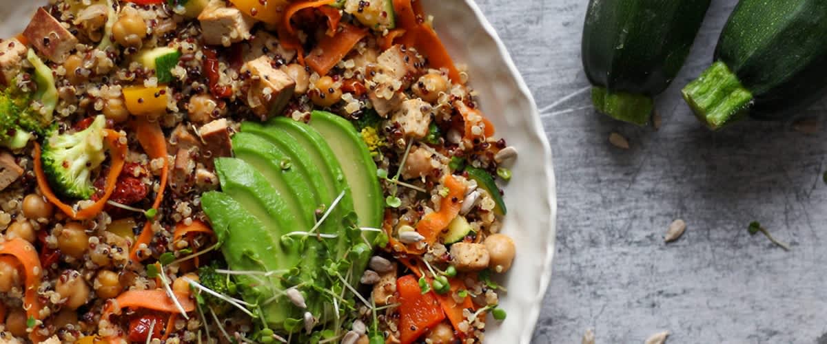 Salát s avokádem, brokolicí, tofu, mrkví, paprikou a cuketou na šedém pozadí