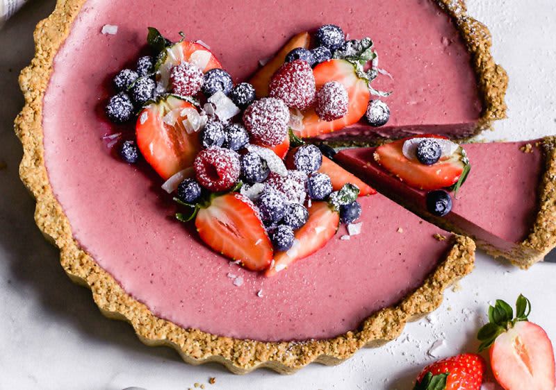 Ovocný koláč s jahodami, borůvkami a malinami posypaný moučkovým cukrem na světlém pozadí