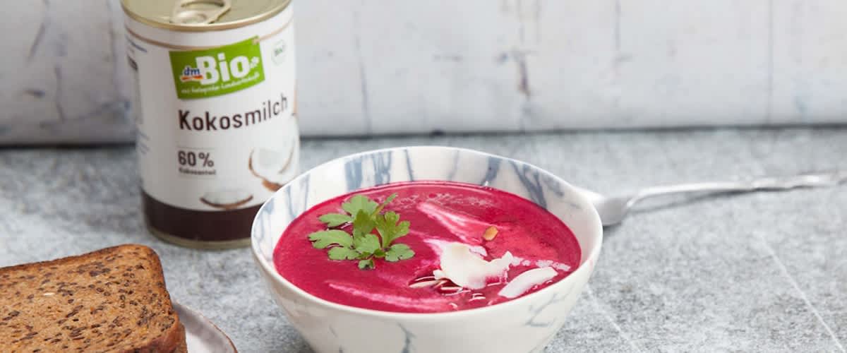 Polévka z červené řepy v misce, kokosové mléko v plechovce, plátky chleba na talíři