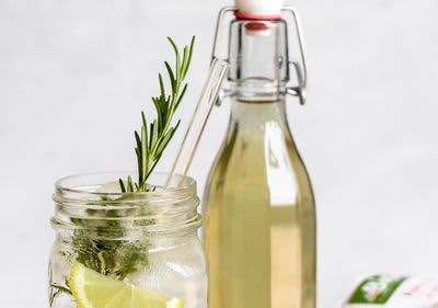 Sklenice s limonádou a rozmarýnem vedle láhve s nápojem na světlém pozadí