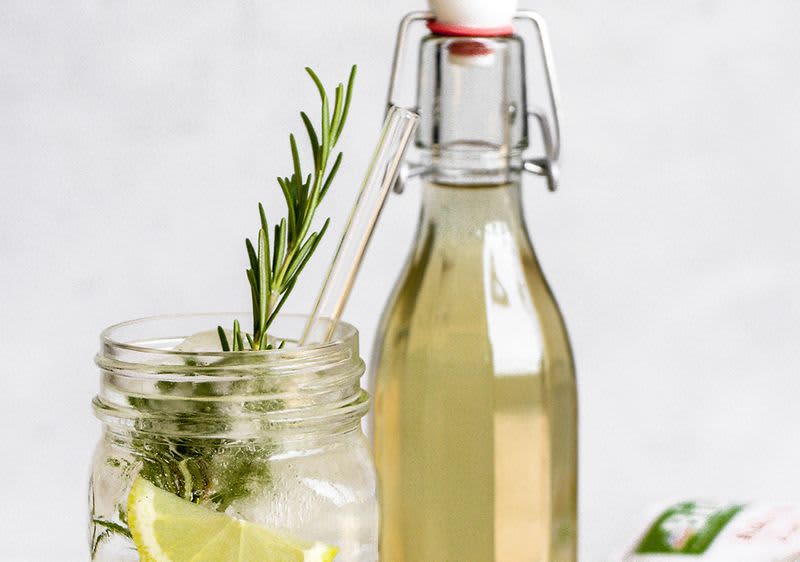 Sklenice s limonádou a rozmarýnem vedle láhve s nápojem na světlém pozadí