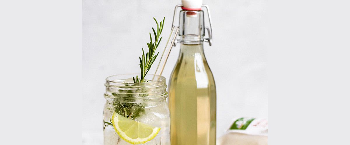 Sklenice s citronem a rozmarýnem vedle láhve s nápojem