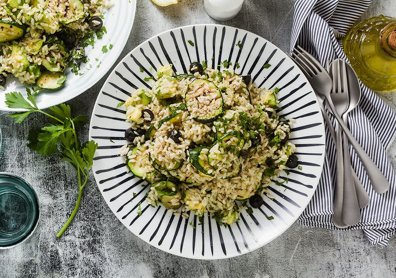 Talíř rizota s cuketou a olivami na stole s příbory a sklenicí vody