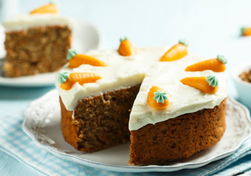 Mrkvový dort s krémem a ozdobami z marcipánových mrkviček na talíři.