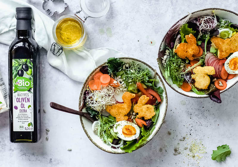 Salát s kuřecími nugetami, vejcem a zeleninou, láhev olivového oleje, sklenice s olejem