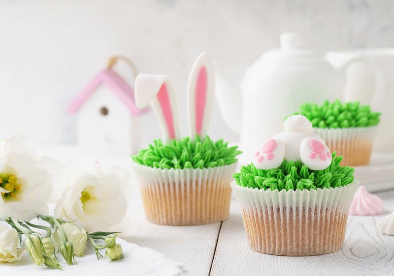 Velikonoční cupcakes s králičími ušima a tlapkami na stole s květinami a konvicí