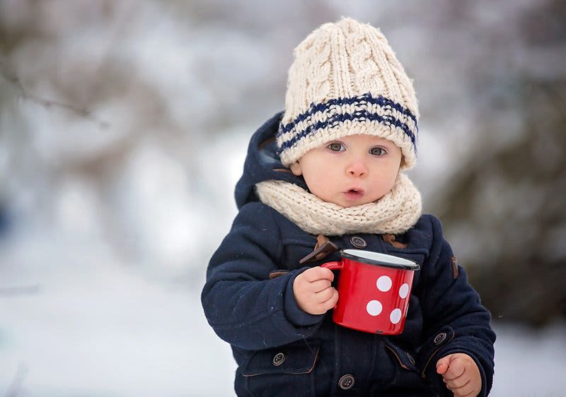 Dítě v zimním oblečení držící červený hrnek s puntíky